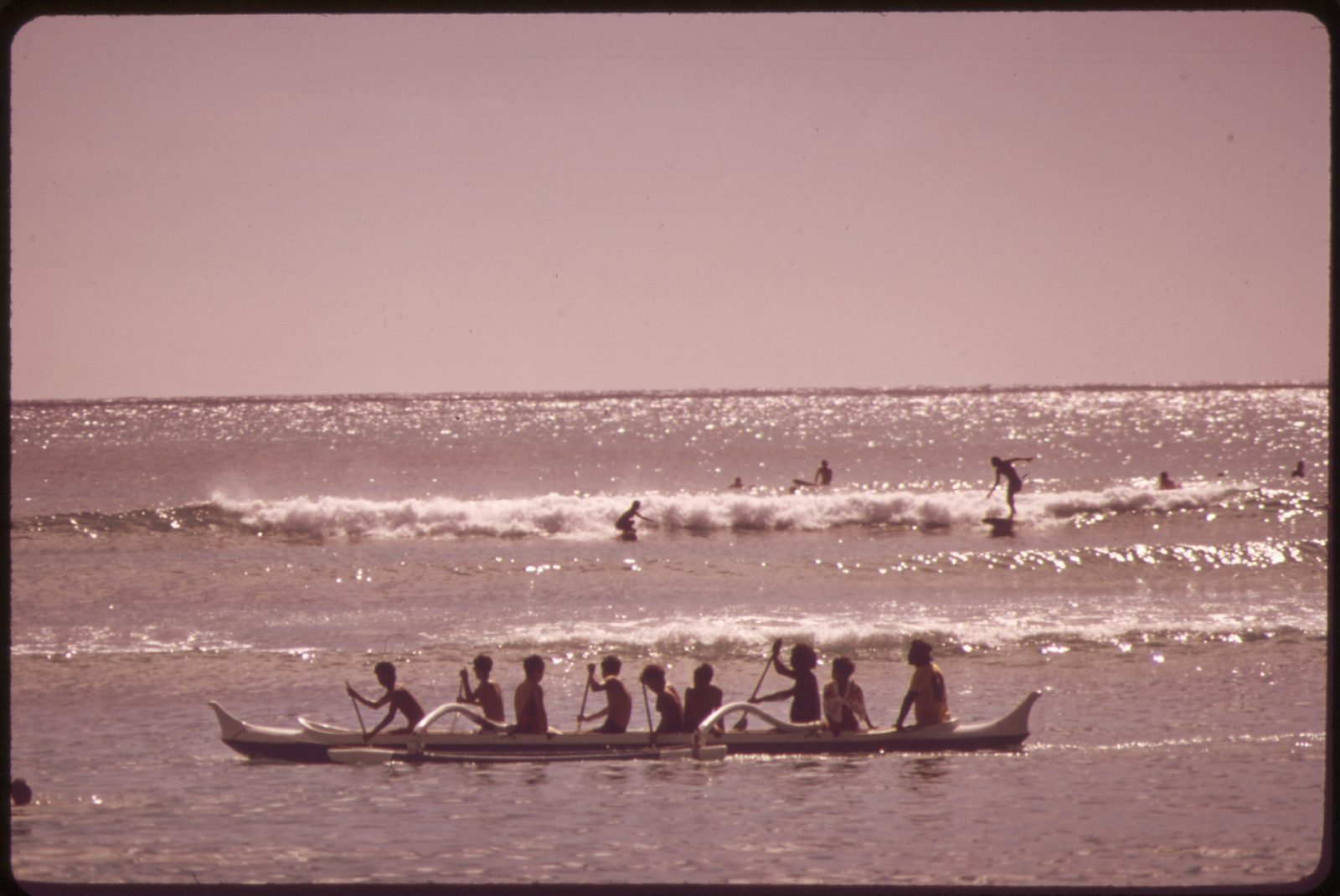 An outrigger canoe crew off Waikīkī Beach with surfers behind
